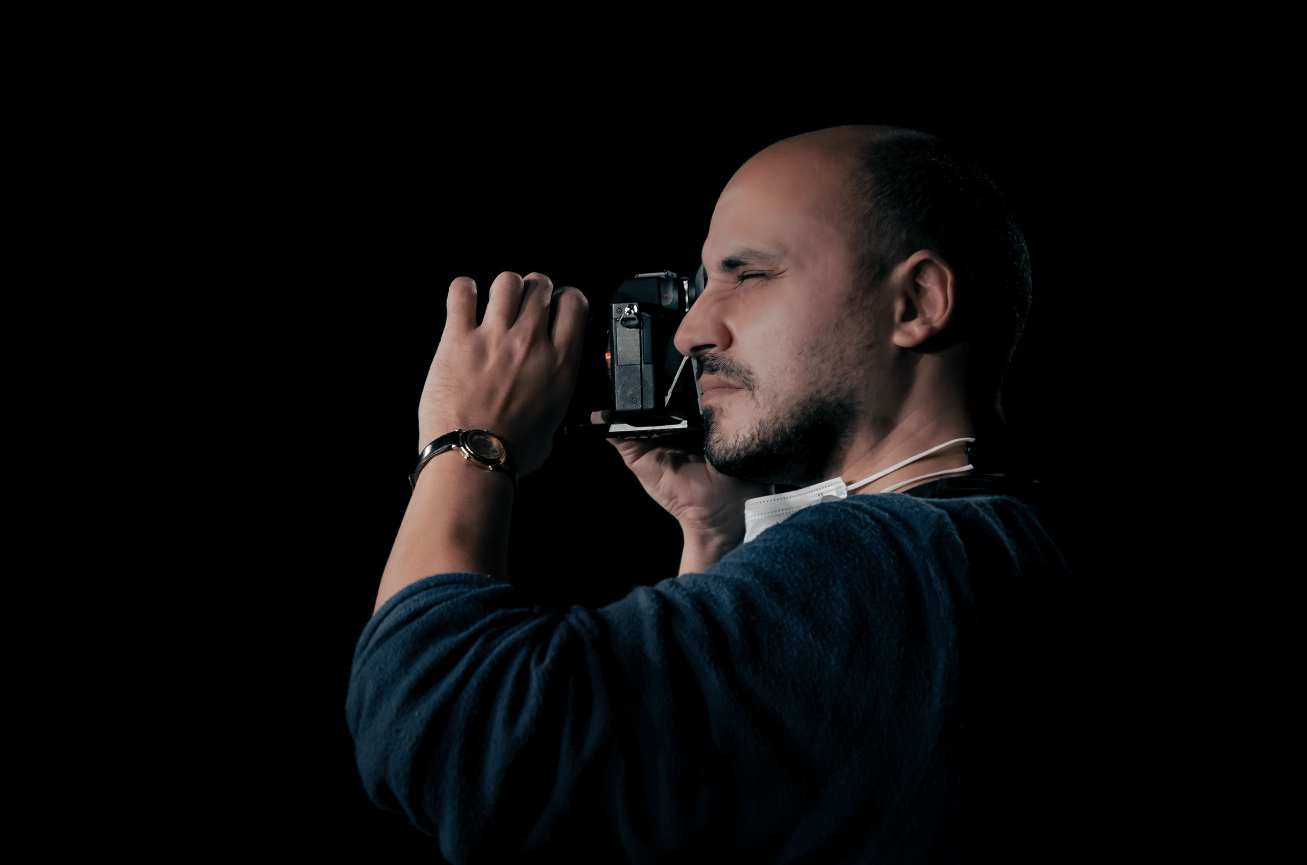 Anouar Brissel — portrait, camera in hand, lit against black